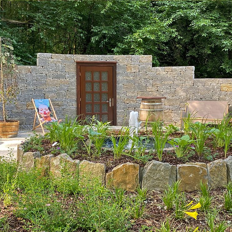 Ein Garten mit einem Steinbeet und im Hintergrund ist eine Tür in einer Steinmauer